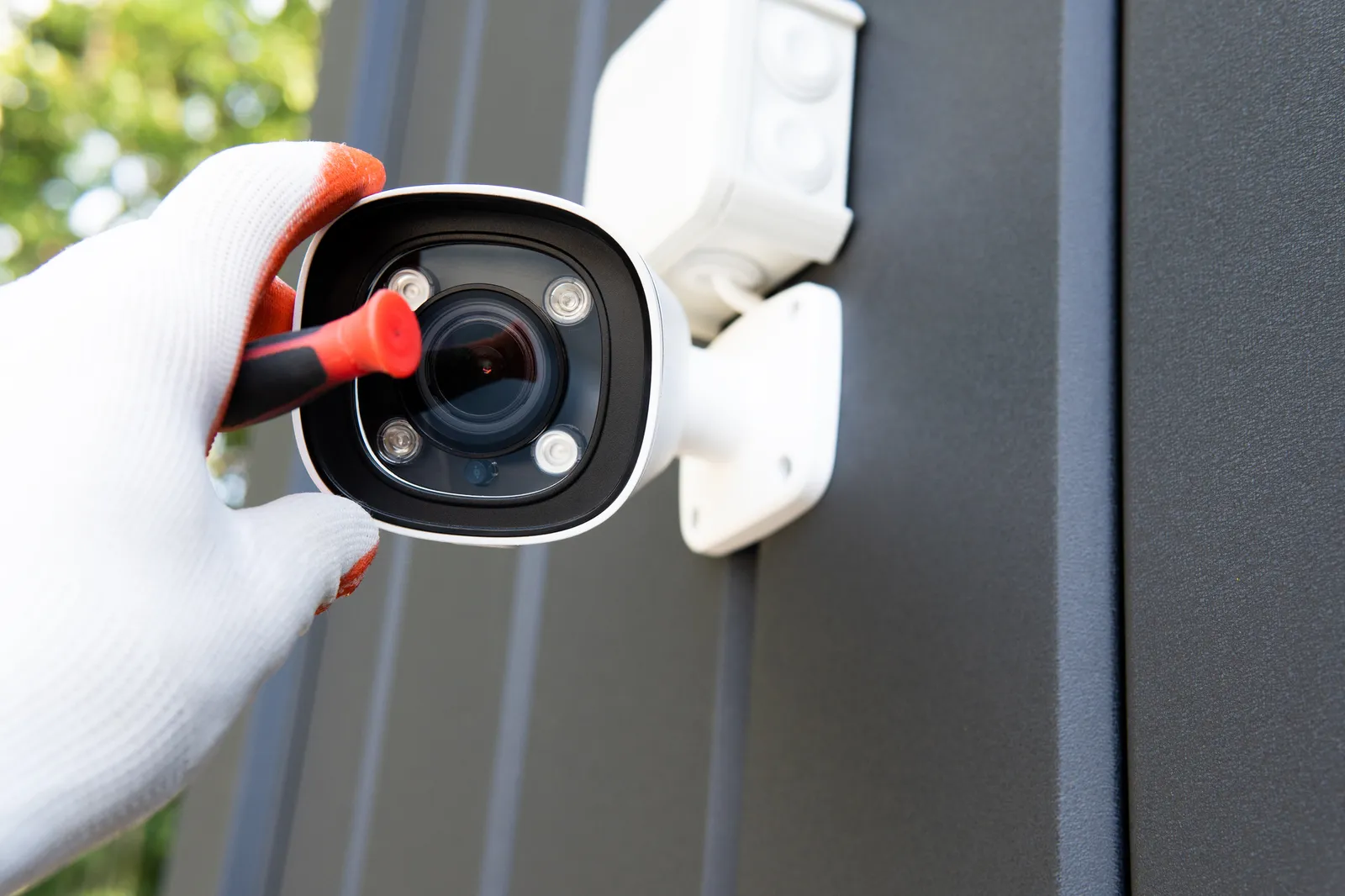 Técnico instalando cámara de vigilancia CCTV con destornillador, primer plano de manos