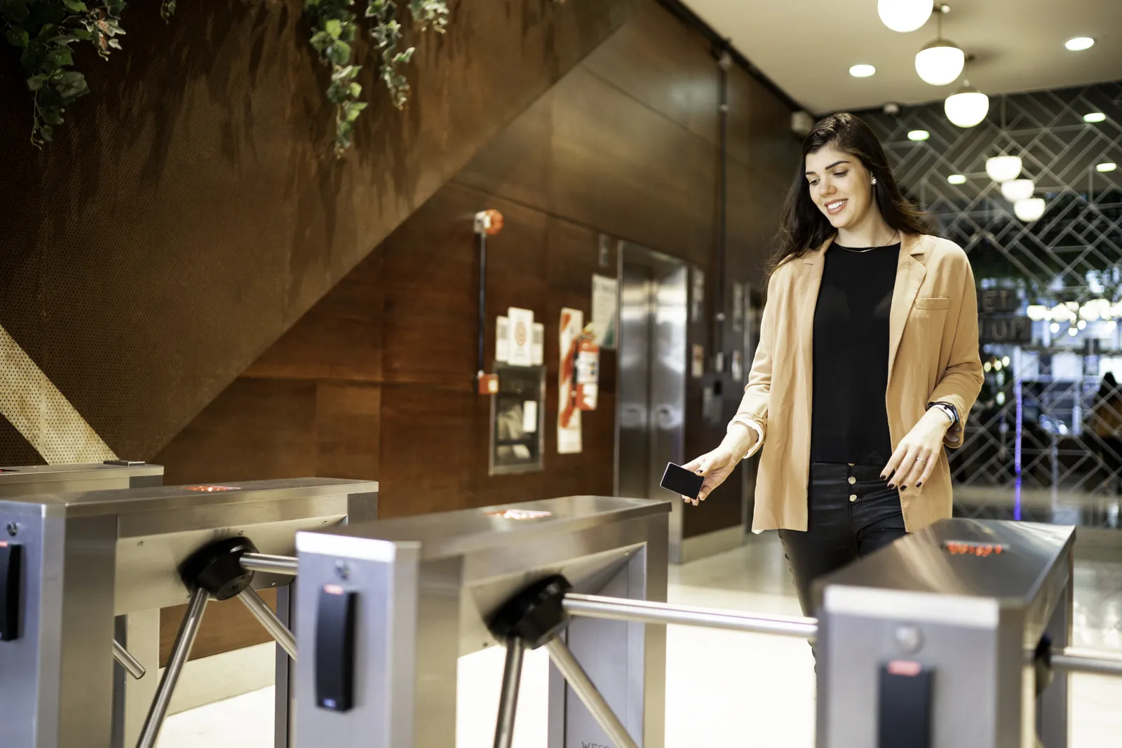 Empleada pasando por torniquete de control de acceso en lobby de oficina corporativa moderna
