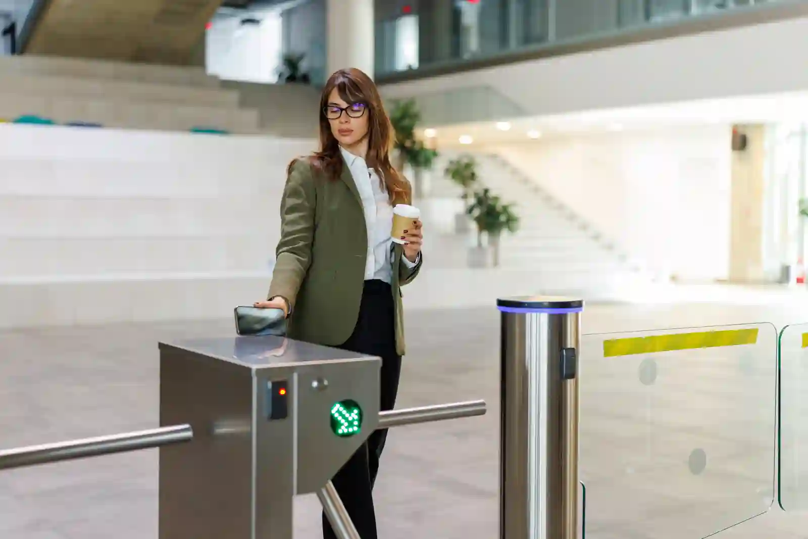 Empleada corporativa pasando por molinete de control de acceso en lobby de oficinas con luz verde de validación