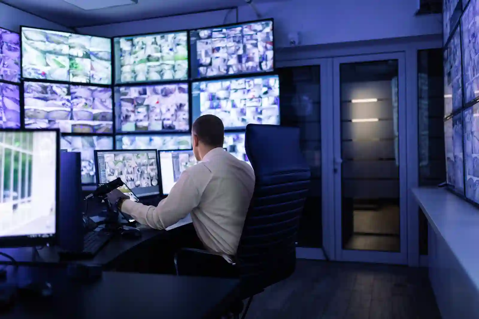 Operador en central de monitoreo 24/7 frente a pared de pantallas con cámaras CCTV corporativas