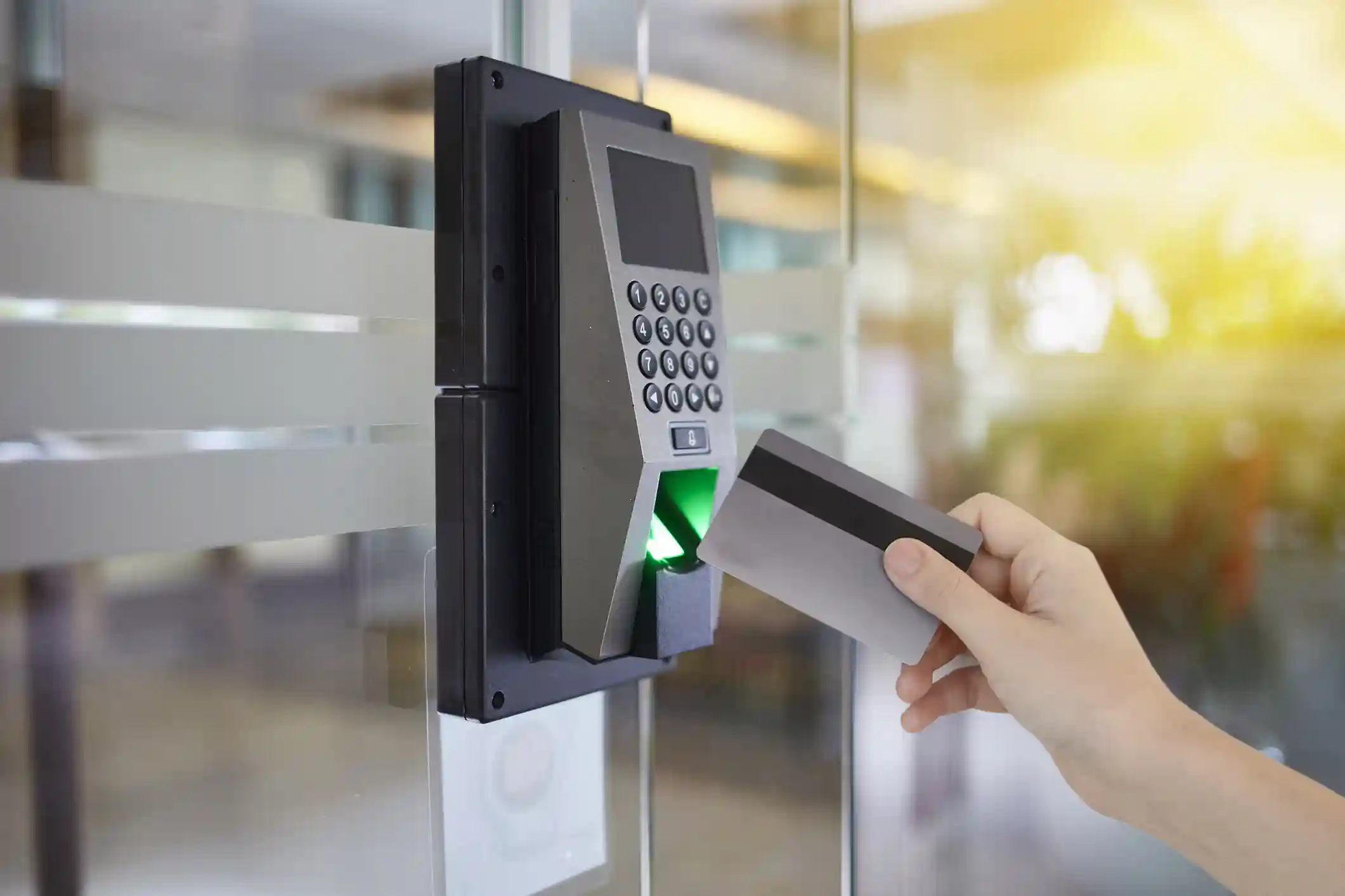 Persona usando una tarjeta de acceso sobre un lector biométrico con teclado numérico en la entrada de una oficina