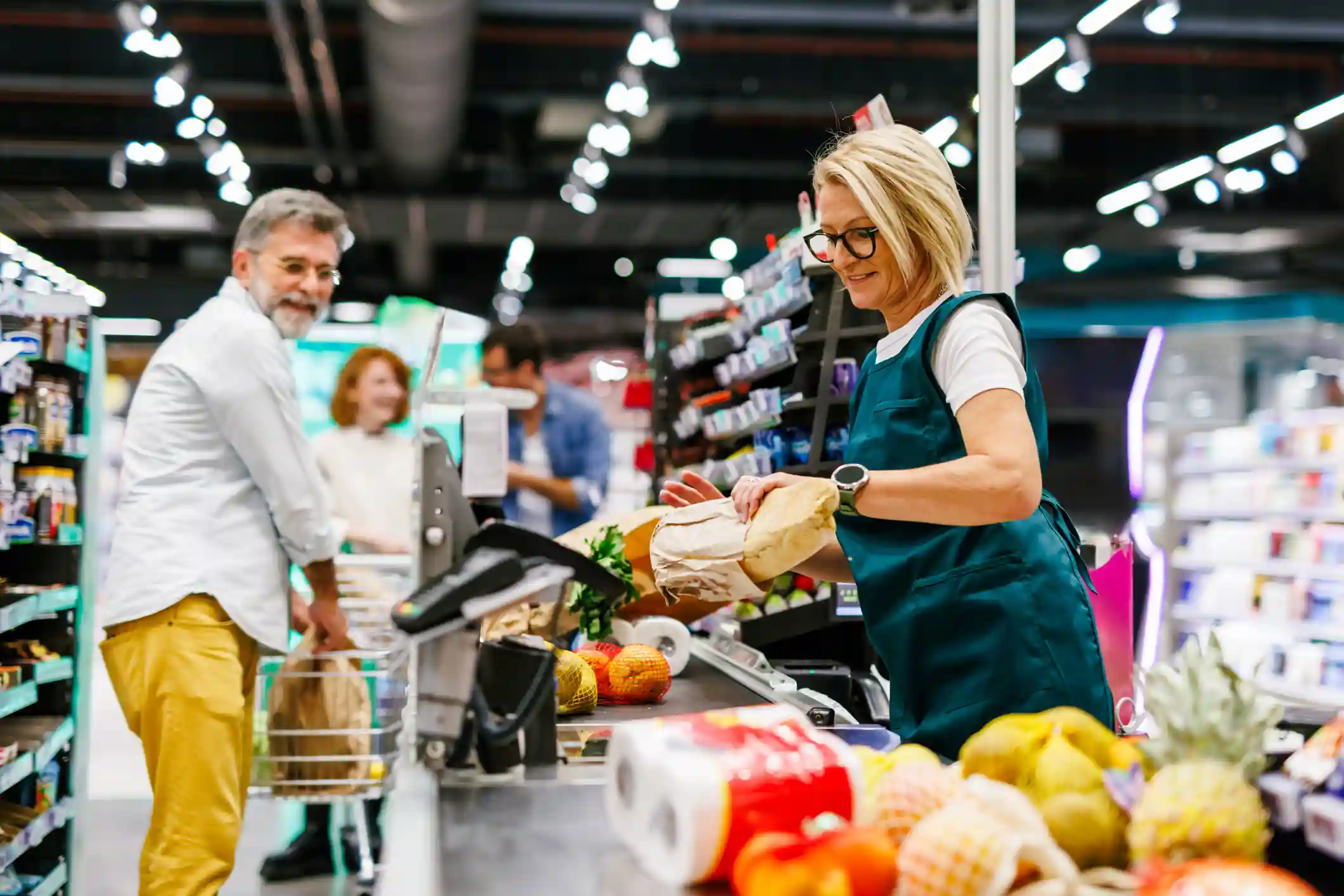 Cajera atendiendo a clientes en la zona de cajas de un supermercado