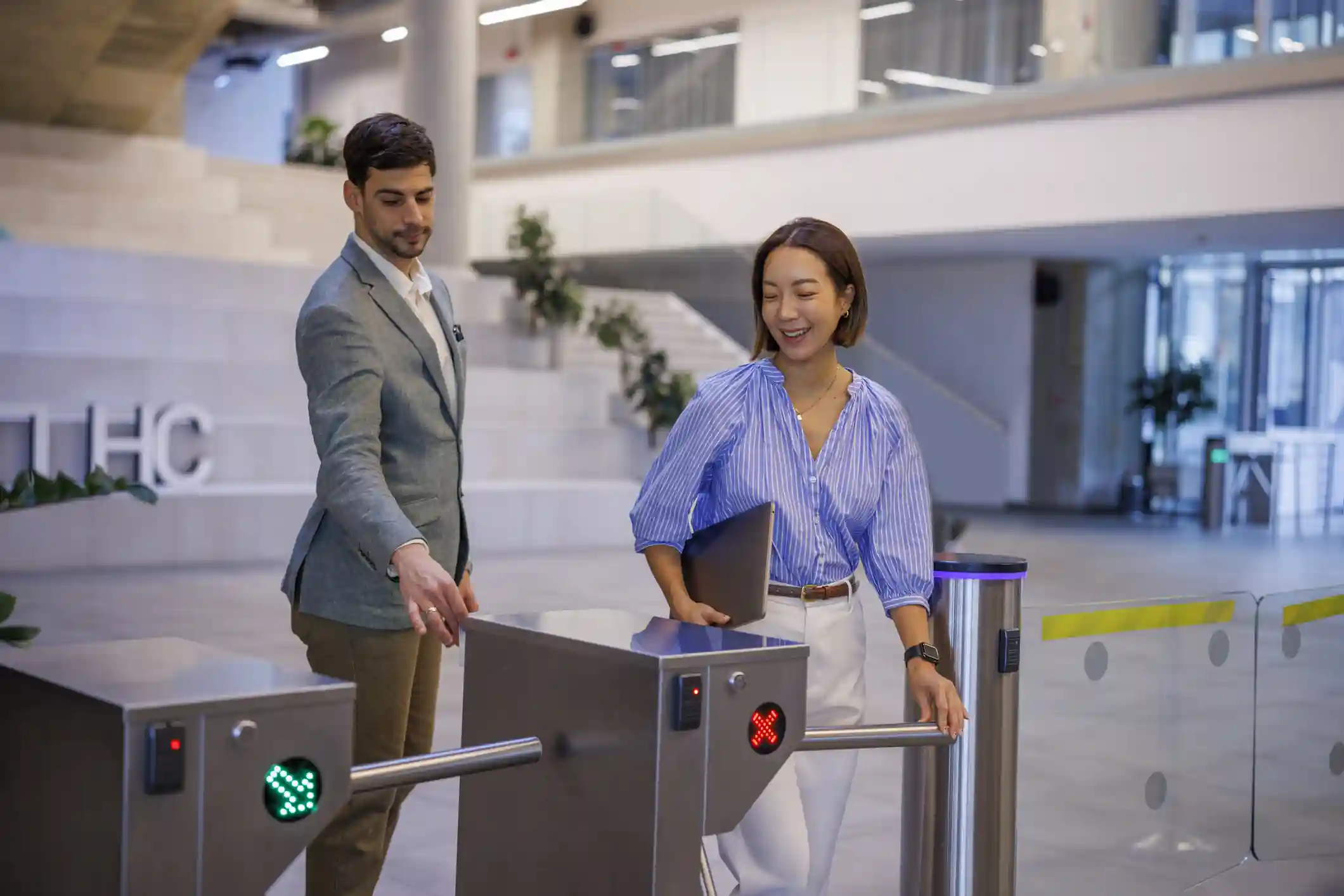 Dos personas pasando por los molinetes de control de accesos en el hall de un edificio corporativo