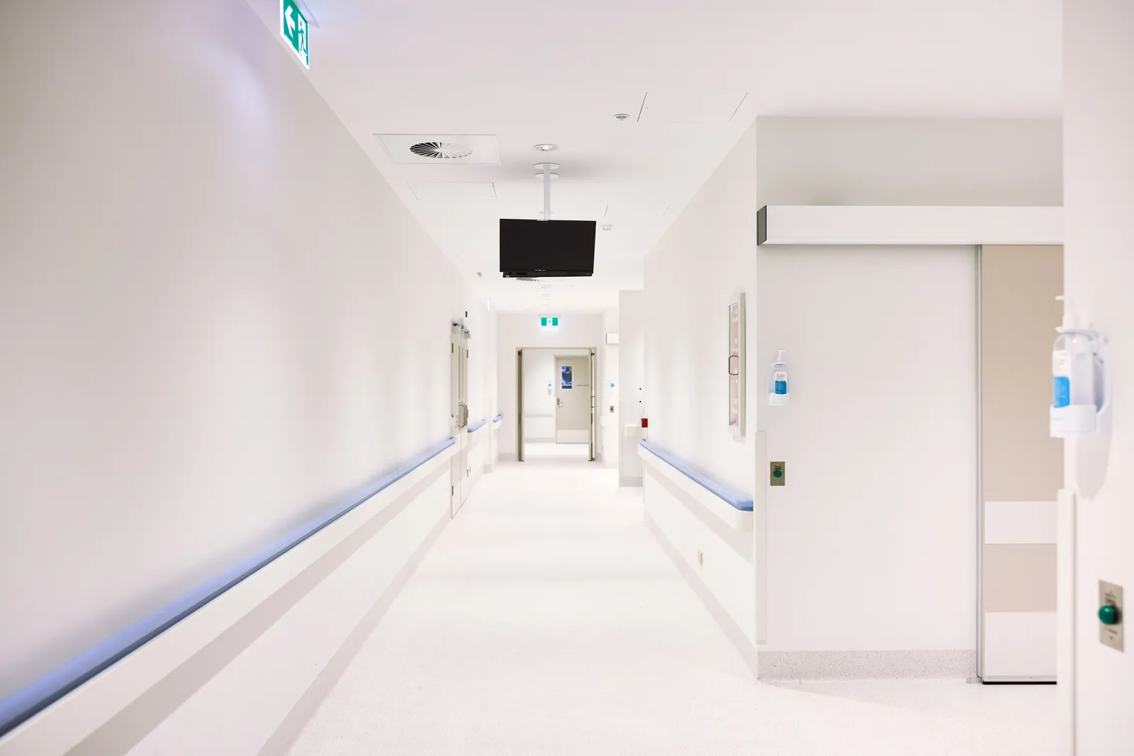 Pasillo interno de una clínica con la puerta corrediza de un sector restringido y señalización de salida de emergencia