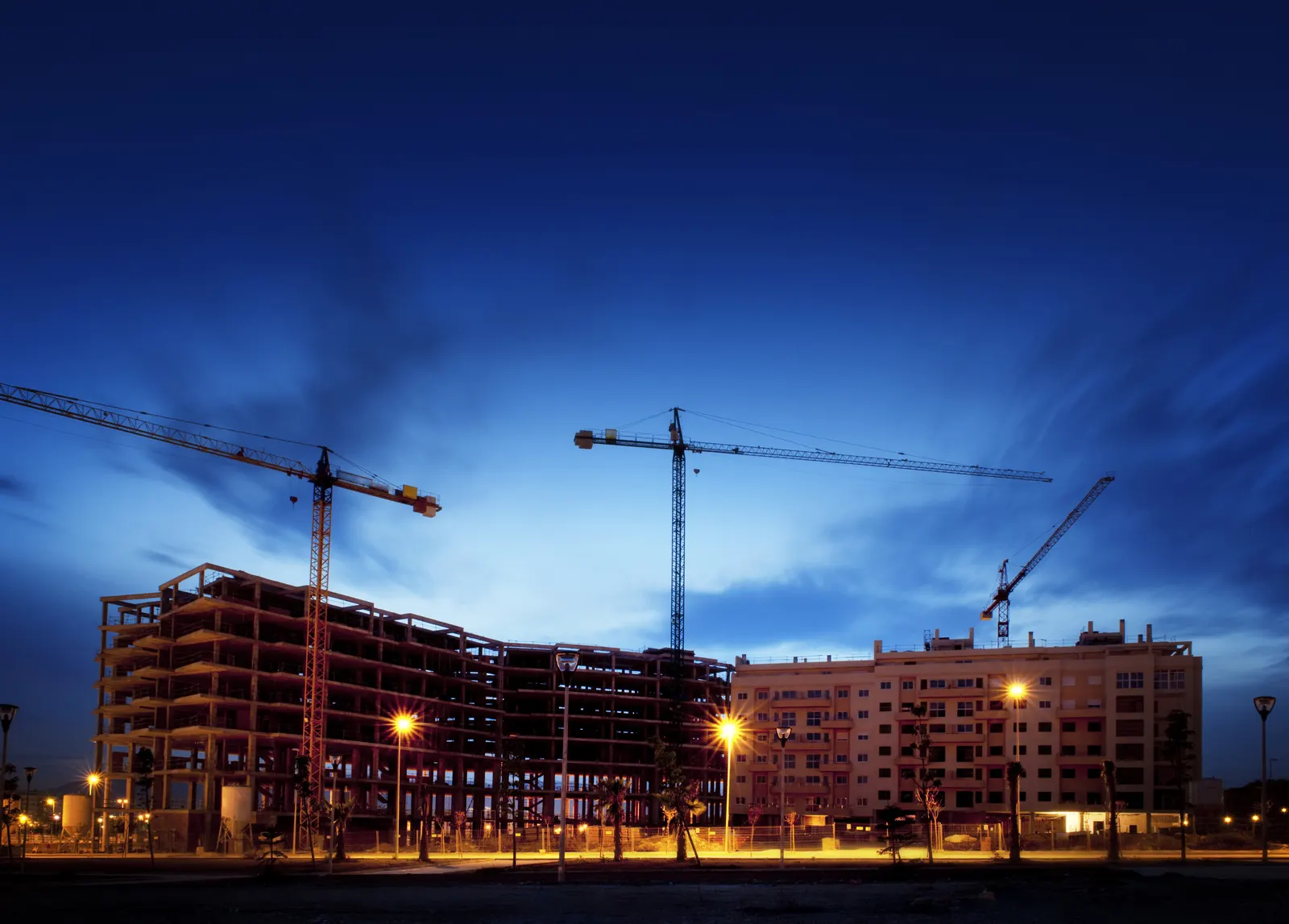 Edificio en construcción con grúas torre iluminado al anochecer