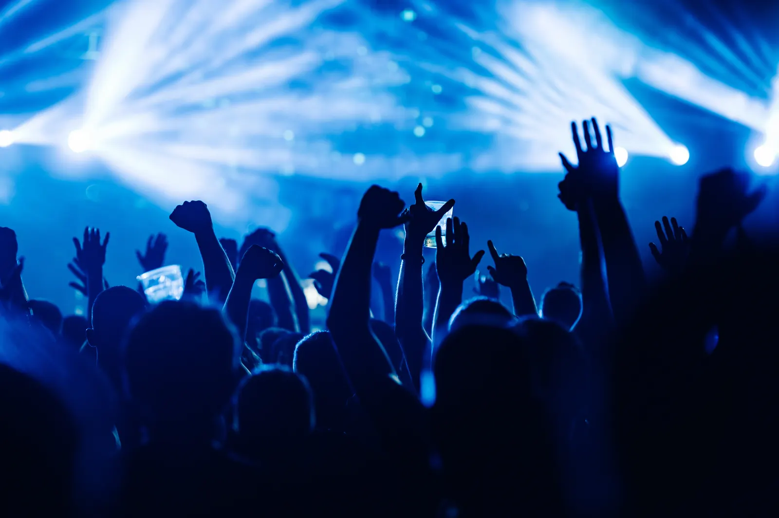 Público con las manos en alto frente a las luces del escenario en un recital