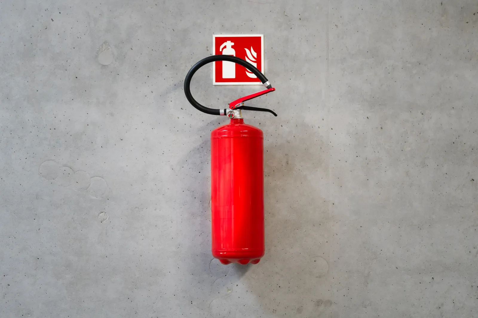 Matafuego rojo colgado en una pared de hormigón con su cartel de señalización