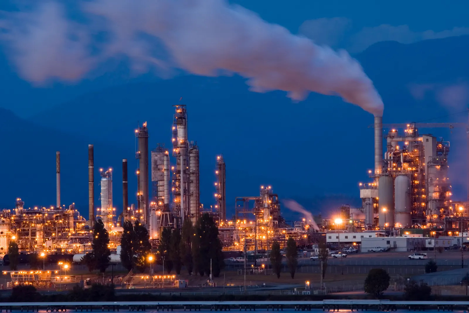 Planta petroquímica iluminada al anochecer con chimeneas y torres de proceso