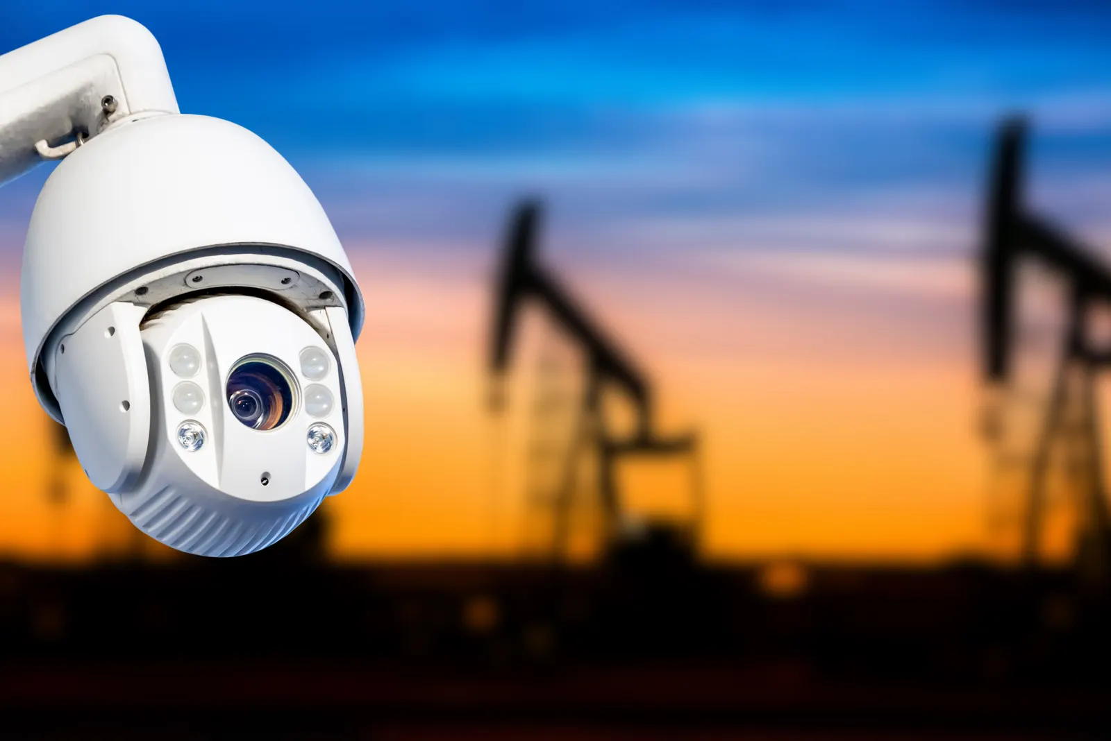 Cámara de seguridad domo con equipos de bombeo de petróleo al atardecer de fondo