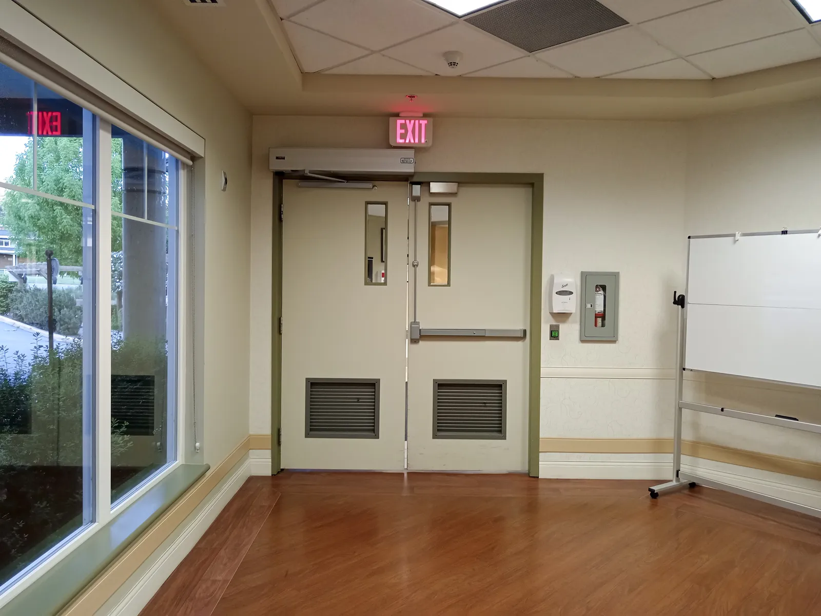 Puerta doble cortafuego con barra antipánico y cartel de salida en un pasillo de hospital