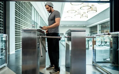 Hombre pasando por un molinete de acceso en el hall de un edificio corporativo con el celular en la mano