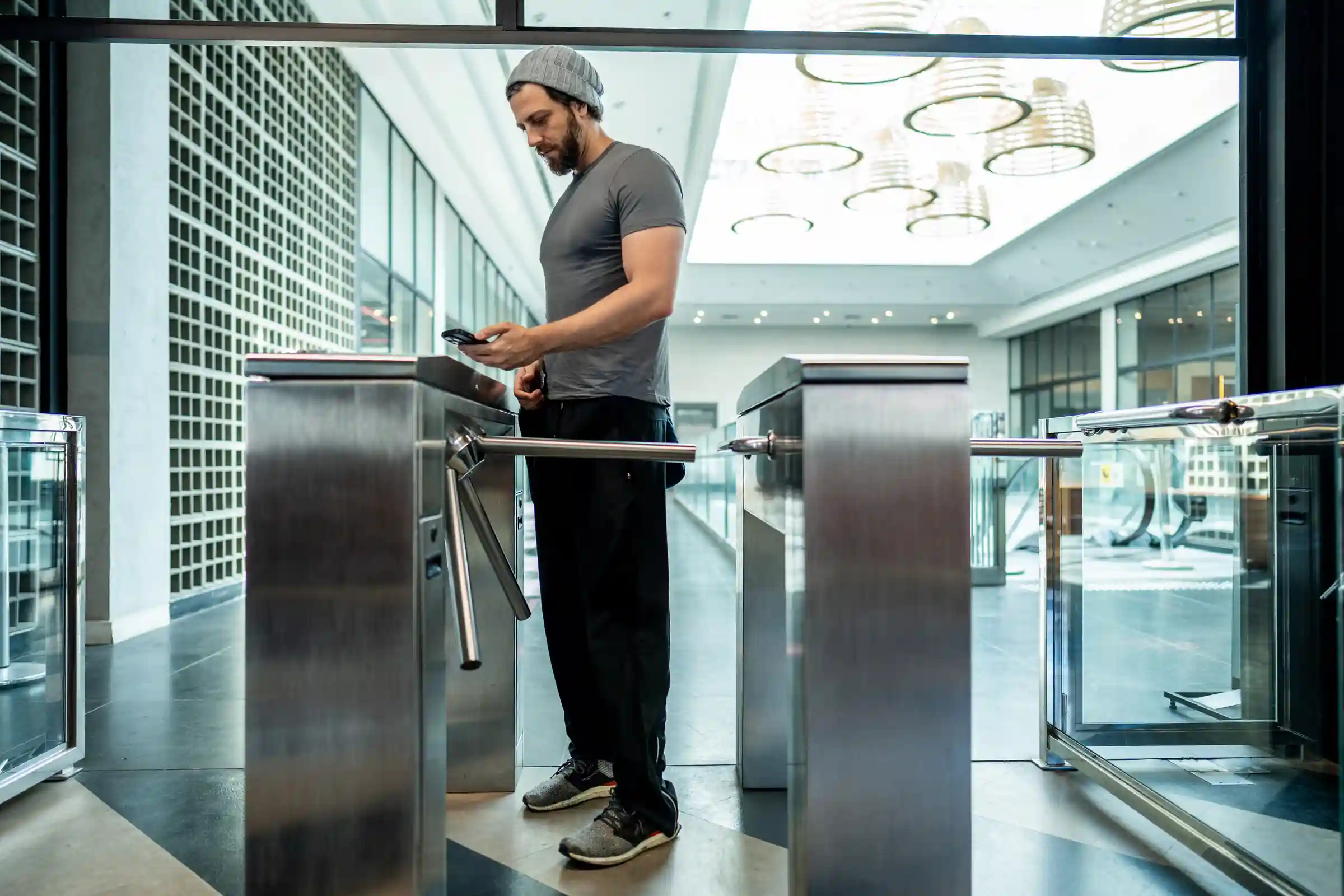 Hombre pasando por un molinete de acceso en el hall de un edificio corporativo con el celular en la mano